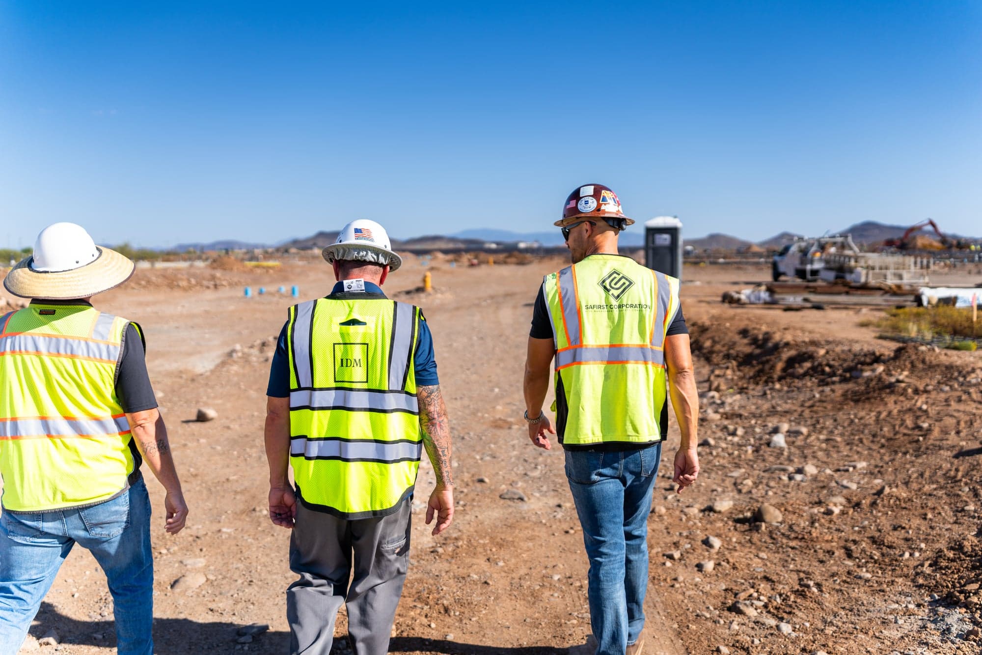 Three safety staff in hi-vis vests and hard hats walking together up a dirt haul road on an earthwork site