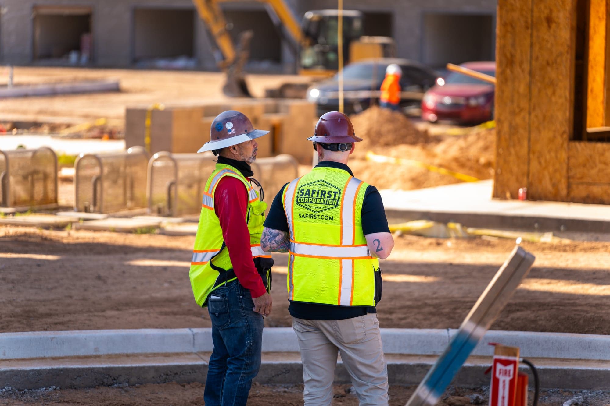 Safety consultant talking with a foreman on a jobsite, a red fire extinguisher on its stand in the foreground