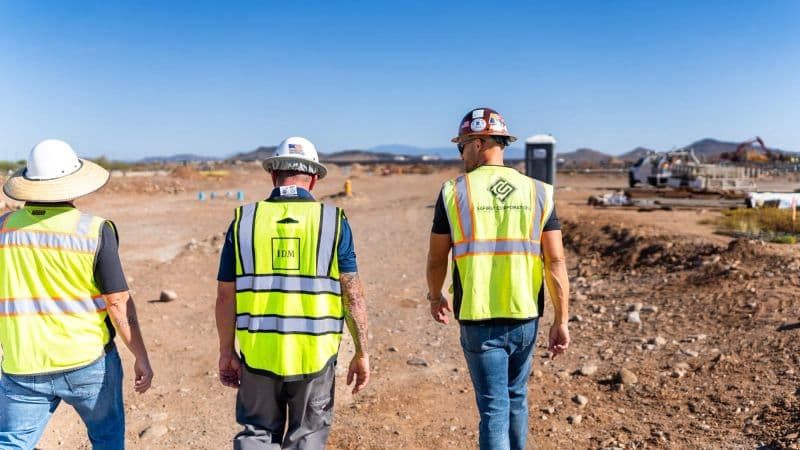 Three men in hi-vis vests and hard hats, backs to camera