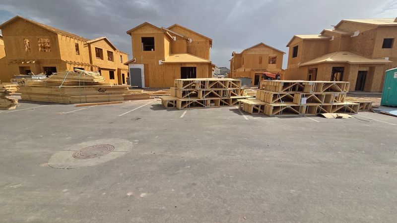 asset-inspection-20260804-b647bda7-5d900994 Open paved area between wood-framed two-story homes under construction, with lumber and roof trusses staged to one side