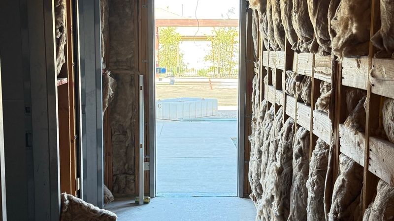 Corridor inside a building under construction, insulation-lined walls leading to an open exit door with daylight outside